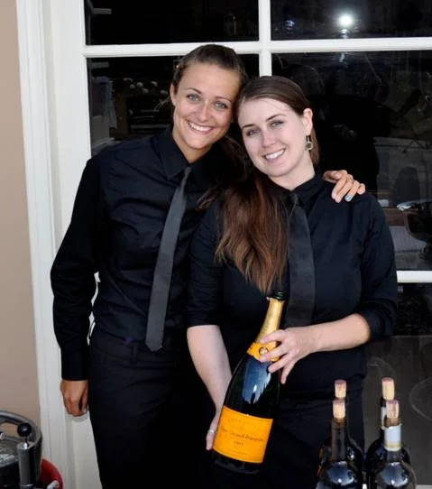 Two professional bartenders in black attire holding champagne at a SoCal private party